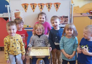 Dzieci prezentują prawie gotową pizzę.